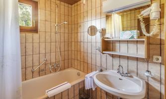 A bright bathroom with tiles, a bathtub, and a sink. There is a window that lets in natural light, as well as a towel rack.