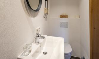 A modern bathroom featuring a white sink and a round mirror. The walls are painted in a bright white, and the floor is dark.