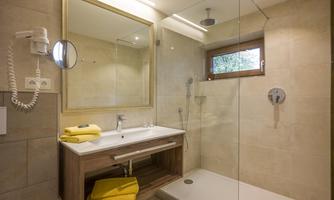 A modern bathroom with a glass shower and a wooden sink. Yellow towels are placed on the sink and a large mirror provides good lighting.