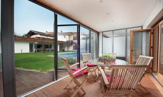 A modern living room with large windows and a view of the garden. There is a table and wooden chairs that create an inviting atmosphere.