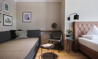 A modern room with a cozy sofa and a bed. Pictures and plants decorate the space, which looks inviting.