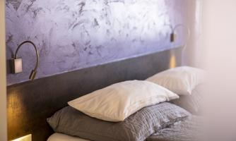 A modern bedroom with an elegant purple headboard and cozy pillows. The soft lighting creates a relaxing atmosphere.