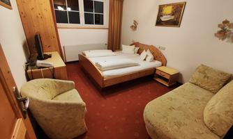 A cozy bedroom with a double bed and a small table. Two armchairs and a television are also available.