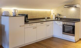 A modern kitchen with white cabinets and wooden flooring. It is well equipped with basic appliances.