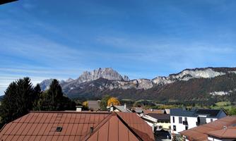 A view of majestic mountains with striking rock formations. In the foreground, rooftops of houses and trees can be seen.