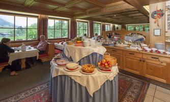 A cozy dining room with wood paneling and large windows. A hearty breakfast buffet with fresh fruit and various dishes is prominently displayed.