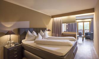 A cozy hotel room with two beds and modern furniture. The room has large windows overlooking a balcony.