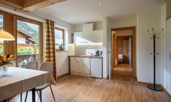 A cozy room with a modern kitchen and a dining table. Large windows let in plenty of light and offer a view of nature.