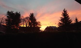 A beautiful sunset with bright colors in the sky. Silhouettes of trees and houses are visible in the foreground.