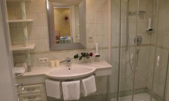 A clean bathroom with a glass shower and a modern sink. The walls are tiled in light colors, and a large mirror reflects the room.