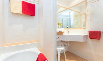 A modern bathroom with a bathtub and a sink. Red towels and a large mirror create an inviting atmosphere.
