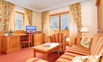 A cozy hotel room with a sofa, a table, and a television.  
Large windows let in plenty of light and offer a view outside.