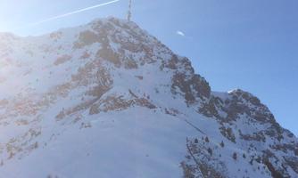 A snow-covered mountain under a clear blue sky. In the foreground, empty wooden tables are visible.