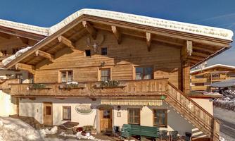 A traditional wooden house in the snow, surrounded by mountains. The clear sky and the white winter landscape give the scene a tranquil atmosphere.
