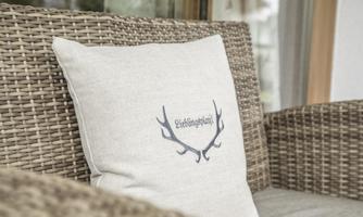 A decorative cushion with the inscription "Favorite Place" and an antler motif. It is lying on a braided couch.