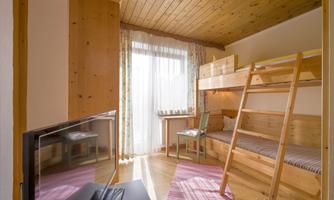 A cozy bedroom with a wooden loft bed and a small table. Large windows let in a lot of light and create a friendly atmosphere.