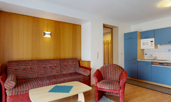 A cozy living room with a red sofa and an armchair. The kitchen is designed in a modern style, with blue cabinets and a small table.