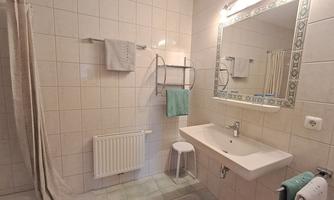 A bright bathroom with white tiles and a modern sink. Towels and a chair complement the decor.