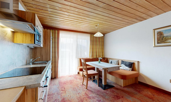 A modern kitchen with bright wooden interior and a dining area. The large window front ensures plenty of daylight.