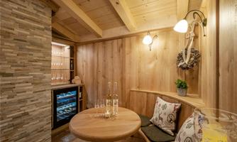 A cozy room with wooden walls and a round table. In the background, there is a small refrigerator and a decorative wall with stone elements.