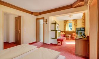 A spacious hotel room with two single beds, a cozy living area, and large windows. The decor is bright and inviting, with warm colors and wooden details.