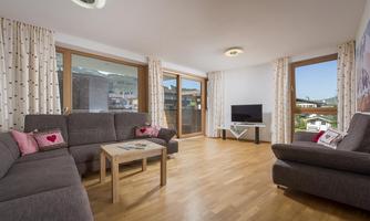 A modern living room with comfortable sofas and a wooden table. Large windows provide plenty of daylight and a view outside.
