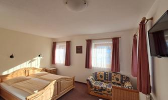 A cozy room with a double bed and a couch. The large windows provide plenty of daylight.