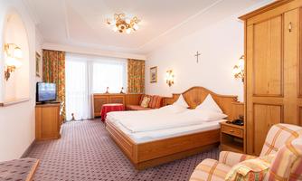A cozy hotel room with a large bed, a couch, and a television. The walls are decorated with stylish curtains and wooden furniture.