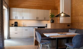 A modern kitchen with wooden paneling and light-colored furniture. The dining area is cozily furnished and provides space for several people.