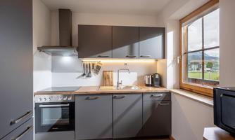 A modern kitchen with gray cabinets and a wooden countertop. The window offers a view of the outdoors.