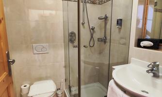A modern bathroom with a glass shower, a sink, and a toilet. The walls are light tiled, and the decor is clean and tidy.