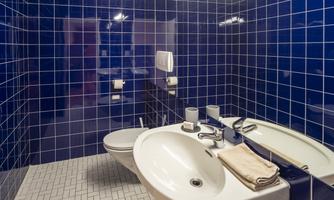 A modern bathroom with blue tiles and a simple decor. There is a sink, a toilet, and towels on the sink.