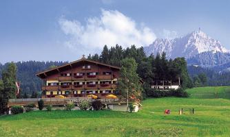 A picturesque hotel in the mountains, surrounded by green meadows. In the background, majestic mountains rise under a clear sky.