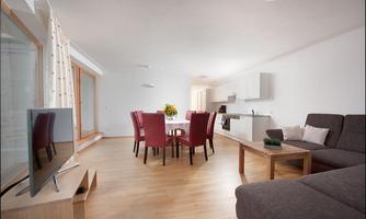 A modern living room with an open kitchen. Red chairs around a table and a cozy sofa bed create an inviting atmosphere.