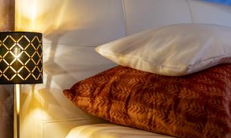 A cozy bedroom with a white bed on which a few pillows are lying. A decorative lamp provides warm light.