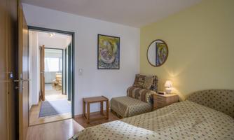 A cozy bedroom with two beds and a small seating area. The walls are light yellow, and there is a round mirror as well as a piece of art.