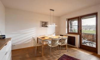 A modern dining room with a wooden table and chairs. Large windows bring in plenty of daylight and offer a view of the outdoors.