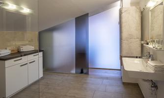 A modern bathroom with a dark wood cabinet and a bright sink. The walls are tiled and there is plenty of natural light.