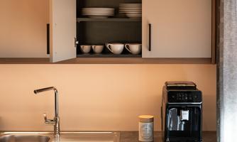 A modern kitchen with cabinets and a sink. On the countertop, there is a coffee machine and dishes are in the shelves.