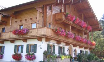 A traditional wooden house with a balcony and many colorful flowers. The facade is bright and inviting.