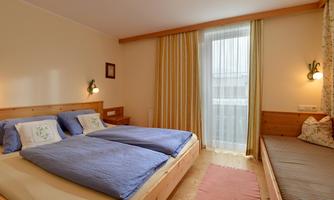 A cozy bedroom with two beds and bright curtains. The room has a balcony and an inviting atmosphere.