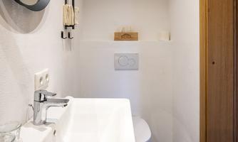 A modern bathroom with a sink, a round mirror, and a toilet. The walls are bright and the floor has dark tiles.
