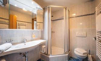 A modern bathroom with a shower cubicle and a sink. Bright tiles and large mirrors create a light-flooded atmosphere.