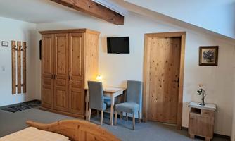 A cozy room with wooden furniture, a bed, and a desk.  
There is a television on the wall and there is a door to another room.