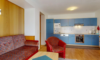 A modern kitchen with blue cabinets and a cozy living area. The furniture is colorful and creates an inviting atmosphere.