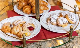 A tiered stand with various pastries, including croissants and fruit-filled pastries. The plates are beautifully arranged and placed on a red cloth.
