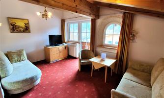 A cozy living room with wooden ceilings and carpeting. There is a television, seating, and a small table.