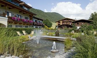 An idyllic hotel complex with blooming balconies and a small pond.  
Relaxed loungers and a bubbling fountain create an inviting atmosphere.