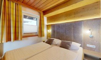 A cozy bedroom with two single beds and wooden ceilings. The room has a window with curtains and modern lighting.
