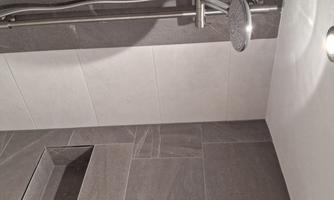 A modern shower with a silver shower head and gray tiles. The walls are partially tiled in light and partially in dark.